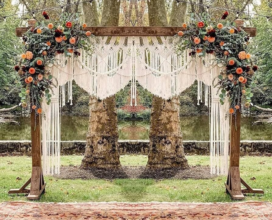 Arco de cerimônia ao ar livre com painel de macramê franjado e arranjos de flores laranja